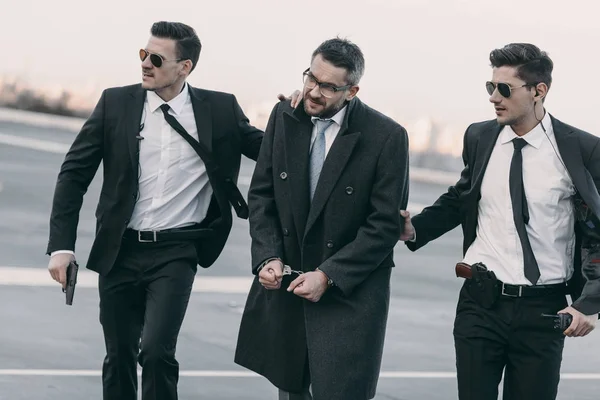 Security guards with guns going with arrested man on helipad — Stock Photo