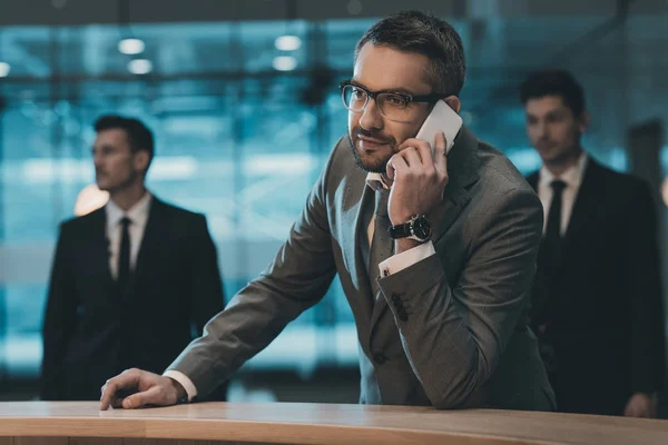 Geschäftsmann spricht per Smartphone und steht am Empfangstresen — Stockfoto