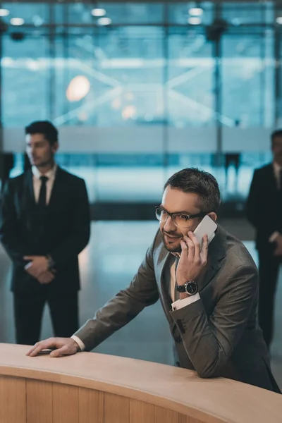 Geschäftsmann steht am Empfangstresen und unterhält sich per Smartphone — Stockfoto