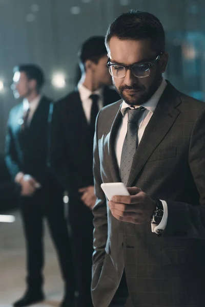 Красивый бизнесмен стоит и смотрит на смартфон — стоковое фото