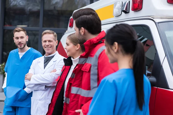 Paramedics working team standing in front of car and looking at each other — Stock Photo