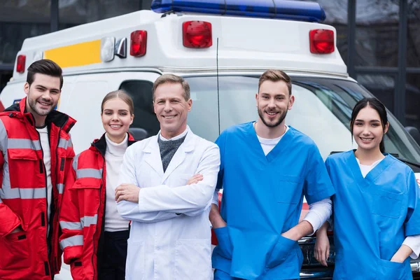 Happy ambulance doctors working team standing in front of car — Stock Photo