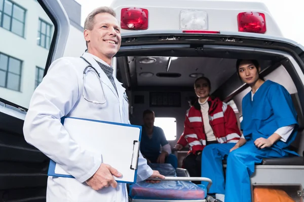 Equipe de trabalho de paramédicos sorridentes com ambulância — Fotografia de Stock