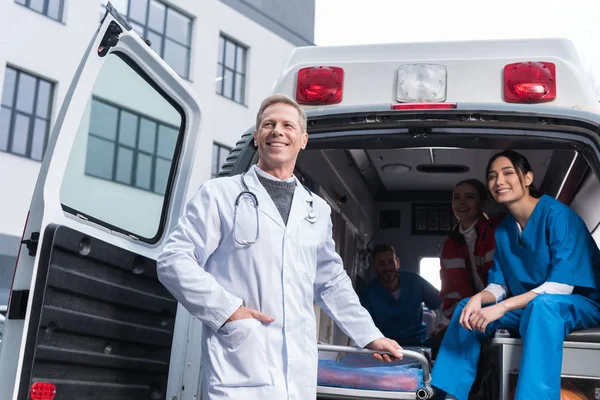 Lächelndes Sanitäter-Team mit funktionierendem Auto — Stockfoto