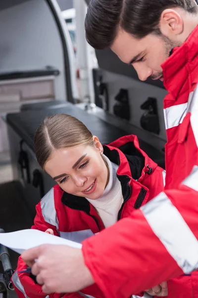 Atraente masculino e feminino paramédicos leitura documentos na frente da ambulância — Fotografia de Stock