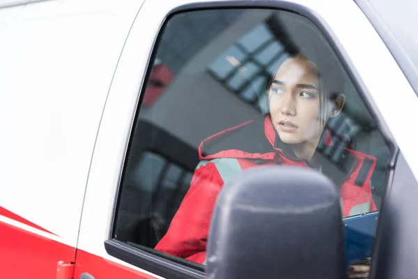 Jovem asiático feminino paramédico sentado em ambulância e olhando para longe — Fotografia de Stock