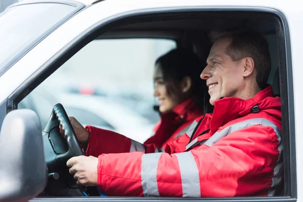 Paramédicos sonrientes masculinos y femeninos sentados en ambulancia - foto de stock