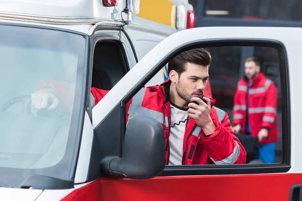 Handsome male paramedic talking by portable radio and standing close to ambulance — Stock Photo