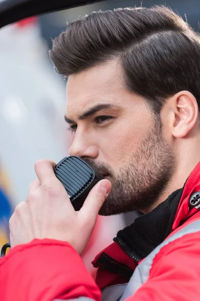 Retrato de un joven guapo paramédico masculino de pie cerca de la ambulancia y hablando por radio portátil - foto de stock