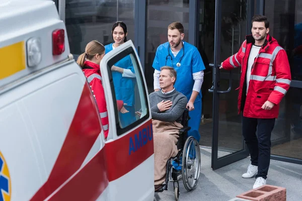 Doctors helping man on wheelchair get to ambulance — Stock Photo