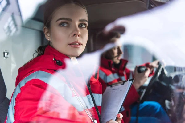 Attractive young paramedic sitting in ambulance and looking away — Stock Photo