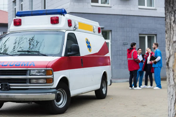 Four ambulance doctors talking and standing near car — Stock Photo