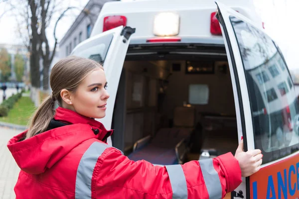 Jeune femme médecin ouvrant les portes de l'ambulance et regardant loin — Photo de stock