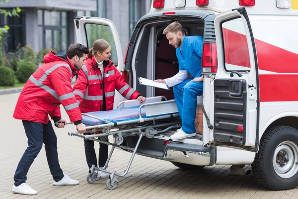 Jovens paramédicos se movendo para fora maca de ambulância de carro — Fotografia de Stock