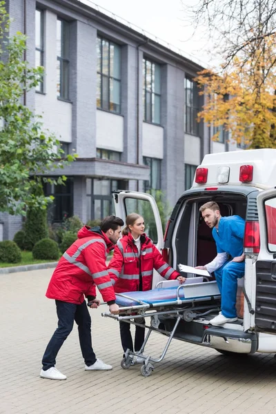 Paramédicos moviendo camilla ambulancia en el coche - foto de stock