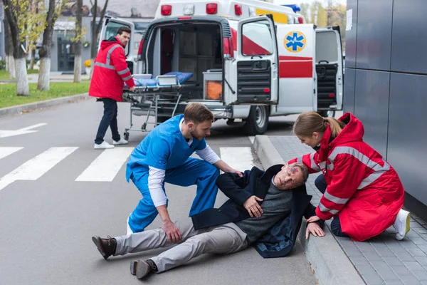 Médicos ayudando a hombre herido acostado en una calle - foto de stock