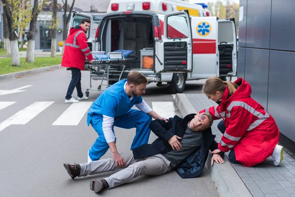 Médicos ayudando a hombre herido acostado en una calle — Stock Photo