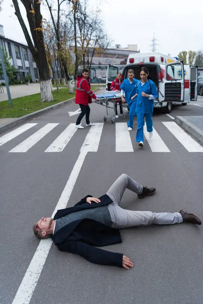 Парамедики бегут, чтобы помочь раненому лежащему на улице — стоковое фото