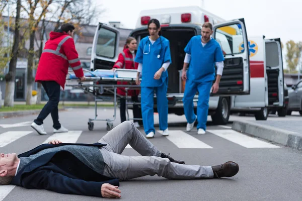 Обрезанный образ врачей, идущих к раненому мужчине средних лет лежащему на улице — стоковое фото