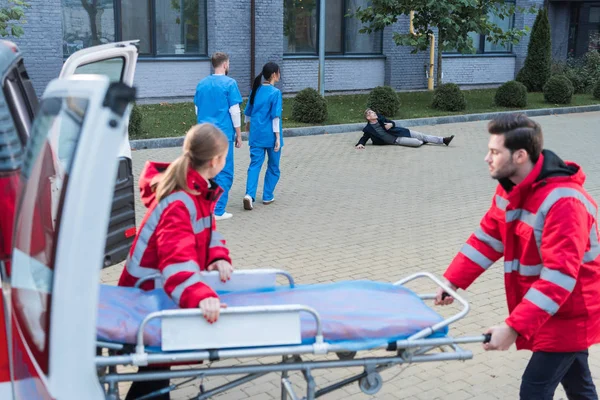 Paramédicos tomando camilla de ambulancia para ayudar a hombre herido - foto de stock