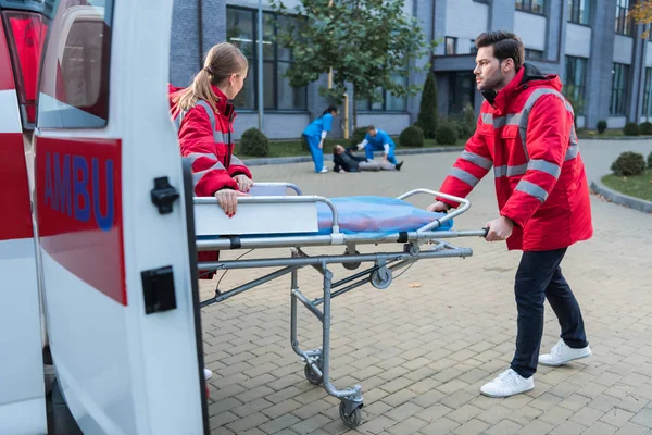 Médicos tomando camilla de ambulancia para ayudar a hombre herido - foto de stock