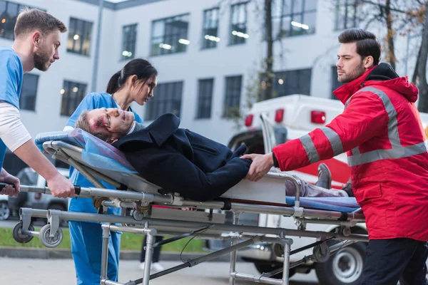 Doctors moving injured man on ambulance stretcher — Stock Photo