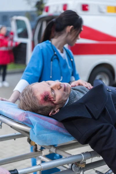 Médico feminino se movendo ferido homem maduro na maca ambulância — Fotografia de Stock