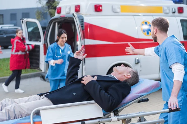 Injured man and doctor asking help of other paramedic — Stock Photo