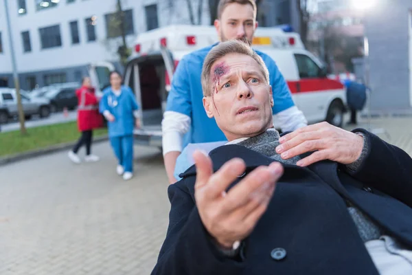 Herido de miedo hombre con herida en la cabeza acostado en la camilla de ambulancia — Stock Photo