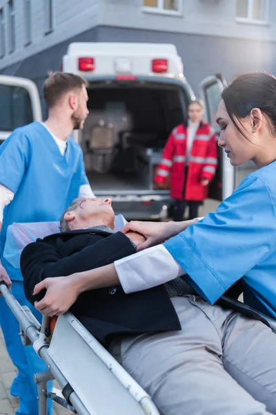 Young paramedics moving wounded man on ambulance stretcher — Stock Photo