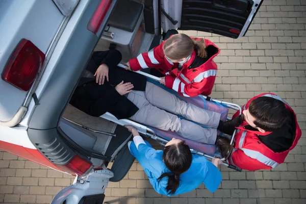 Top view of paramedic team moving man on ambulance stretcher into car — Stock Photo
