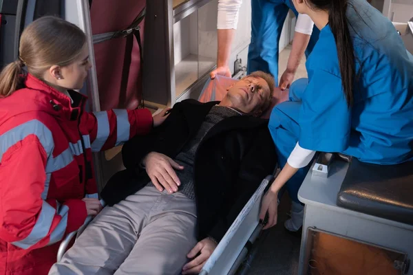 Cropped image of paramedics moving unconscious man into ambulance — Stock Photo