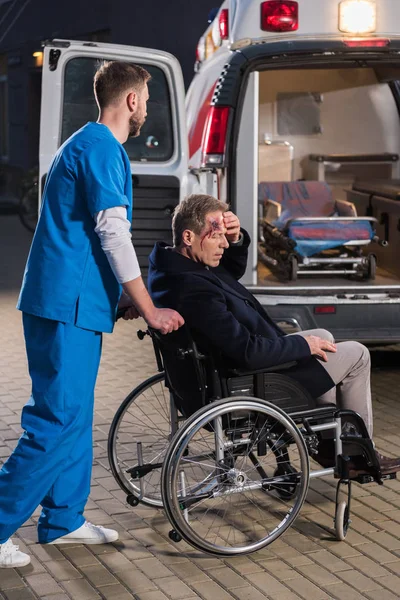 Paramedic moving injured man on wheelchair to ambulance — Stock Photo