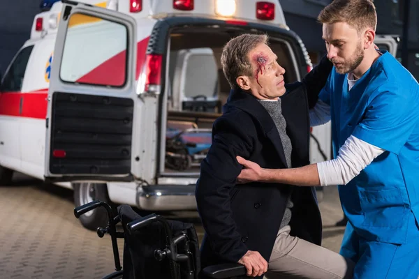 Paramedic helping injured man to sit on wheelchair — Stock Photo