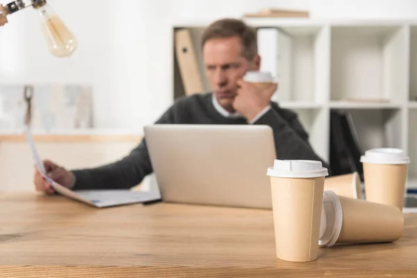 Müder Geschäftsmann mittleren Alters arbeitet mit Laptop und trinkt viel Kaffee — Stockfoto