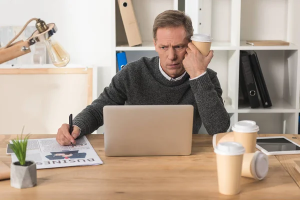 Tired businessman sitting at laptop with disposable coffee cup — Stock Photo