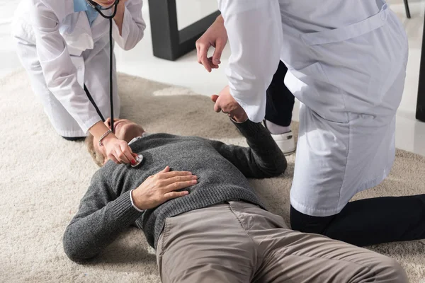 Cropped image of doctor checking unconscious middle aged man palpitation with stethoscope — Stock Photo