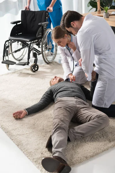 Female doctor checking unconscious man palpitation with stethoscope — Stock Photo