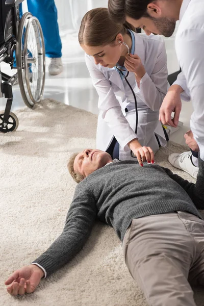 Female doctor checking unconscious middle aged man palpitation with stethoscope — Stock Photo