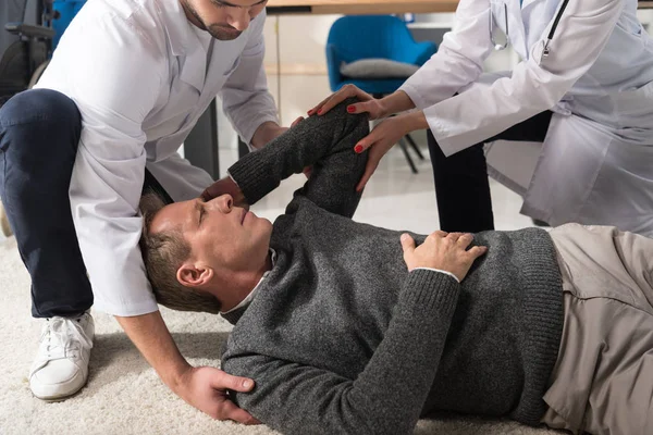 Cropped image of doctors helping fell man — Stock Photo