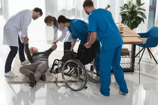 Doctors helping fell mature man to sit on wheelchair — Stock Photo