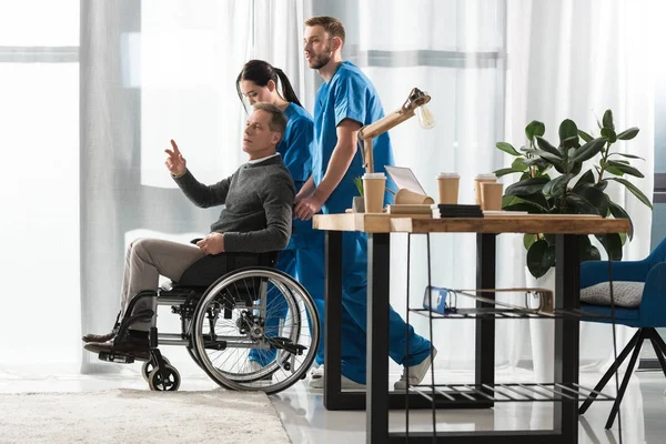 Enfermeras ayudando a hombre de mediana edad en silla de ruedas - foto de stock