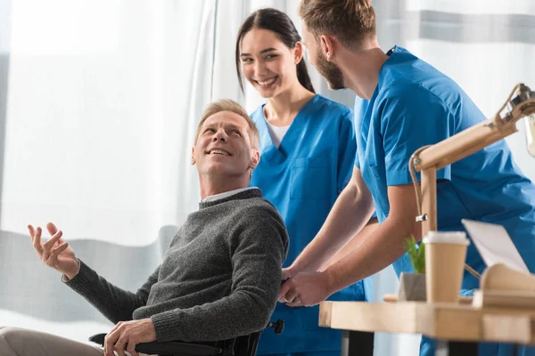 Усміхнені лікарі та пацієнт на інвалідному візку розмовляють у лікарні — стокове фото