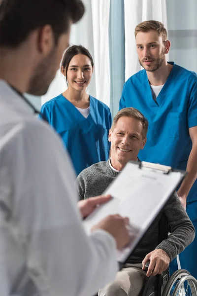 Sorridente paziente maturo sulla sedia a rotelle ascolto medico — Foto stock