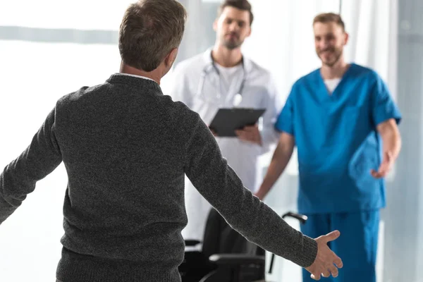 Paciente sano que va con los brazos abiertos a los médicos sonrientes - foto de stock