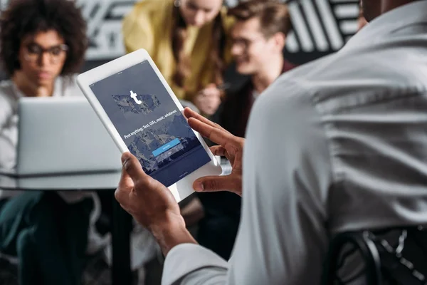 Mann mit Tablet mit Tumblr-App auf dem Bildschirm mit seinen Geschäftspartnern im Hintergrund — Stockfoto