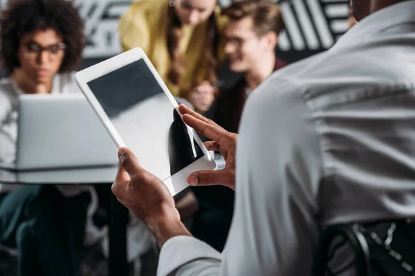 Homem usando tablet com seus parceiros de negócios em segundo plano — Fotografia de Stock