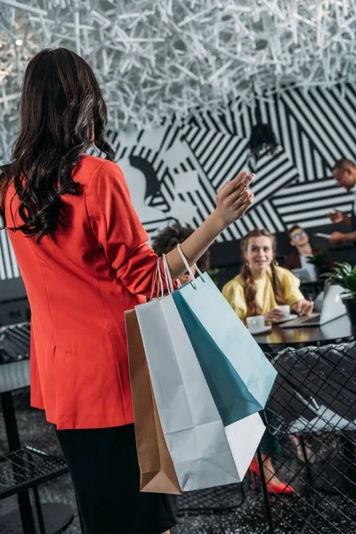Mujer con bolsas de compras va a sus amigos en la cafetería - foto de stock