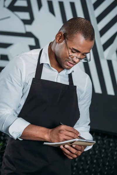 Beau jeune serveur afro-américain écrit dans le bloc-notes — Photo de stock