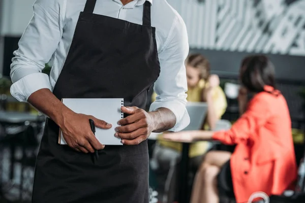 Cropped shot of waiter in apron with notepad at cafe — Stock Photo